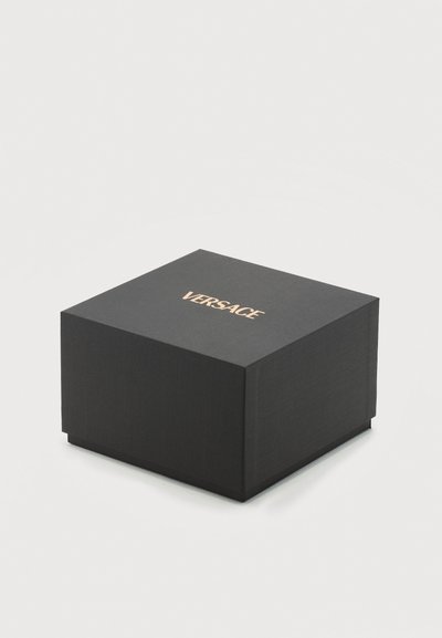 Juodas kvadratinis dėžutės dangtis su auksiniu VERSACE logotipu, uždarytas, ant šviesaus paprasto fono.