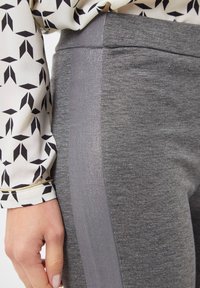 Leggings grises con una textura suave y un panel lateral brillante y reflectante. Detallados con una blusa de manga con un patrón geométrico.