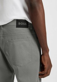 Gray patterned pants with a black "BOSS" label at the waistband, showcasing a fitted design and textured fabric. A hand rests on the side.
