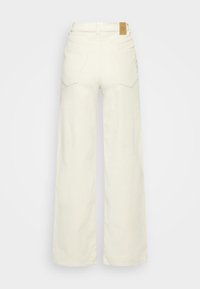 Leveälahkeiset, kermaan väriset farkut, joissa on korkea vyötärö, kaksi taka-taskua ja näkyvä merkkilappu takavyötäröllä.