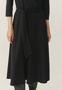 Zwarte jurk met ceintuur, tot op de knie, zacht materiaal, vloeiende snit, met lange mouwen en een strik in de taille voor een aansluitende pasvorm.