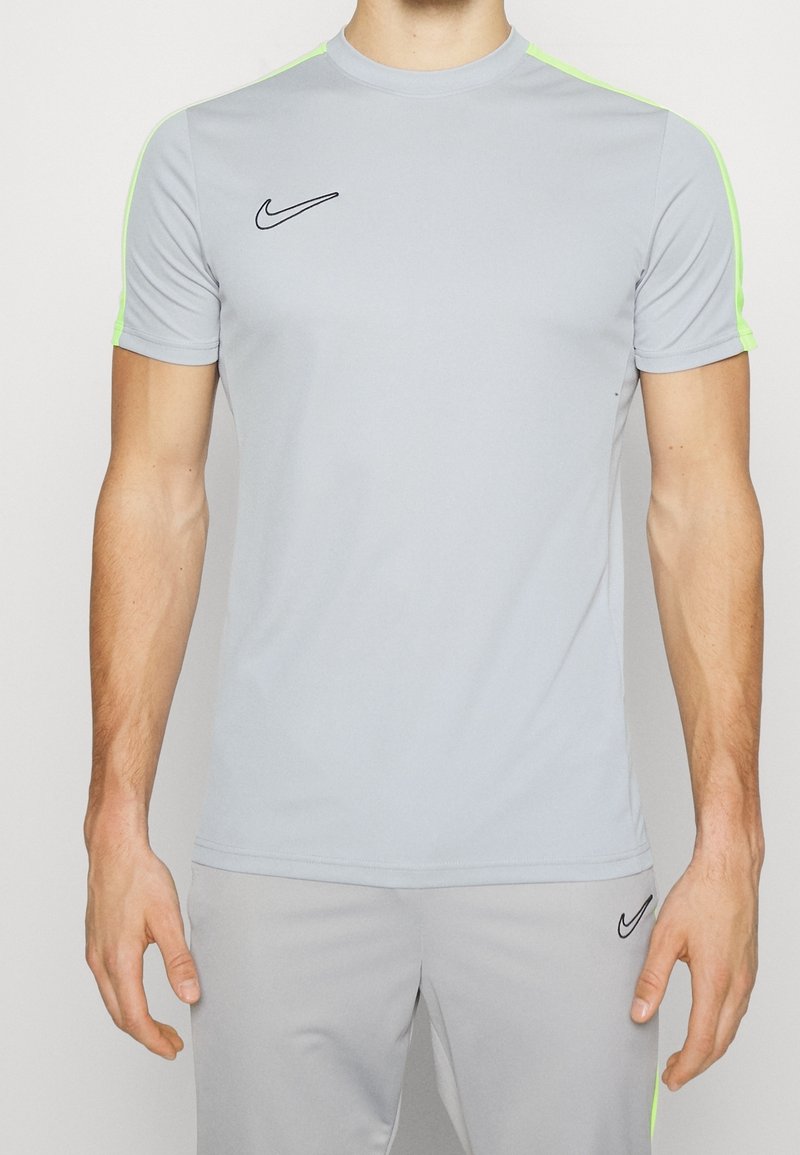 Camiseta atlética gris de manga corta, con acentos en verde neón en los hombros y un logo negro de Nike en el pecho. Tejido elástico y ligero.