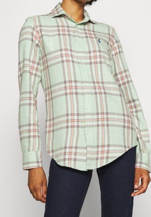 Zielona koszula w kratę na guziki z długimi rękawami. Posiada jasnoszare, różowe i białe paski, zapięcie na guziki z przodu oraz małe logo na piersi.