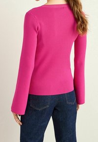 Fitted ribbed long-sleeve top in bright pink, featuring a round neckline and bell-shaped sleeves, paired with dark denim jeans.