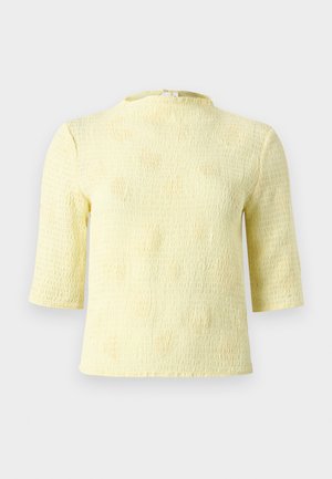 Haut à manches courtes légèrement texturé de couleur jaune pâle avec un col montant et un motif discret de petits pois. Il comporte une fermeture au dos pour un enfilage facile.