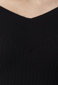 Top nero a coste con scollatura a V e texture verticale. Il tessuto è liscio, con un dettaglio cucito al collo.