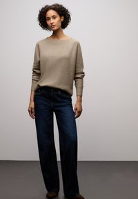 Beżowy wełniany sweter z okrągłym dekoltem i prążkowanymi mankietami w połączeniu z ciemnoniebieskimi jeansami o szerokich nogawkach. Gładka tekstura, casualowy krój.