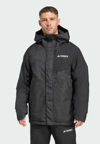 Schwarze isolierte Jacke mit strukturierter Oberfläche, ausgestattet mit einer Kapuze, Reißverschluss und einem kontrastierenden weißen Logo auf der Brust und dem Ärmel.