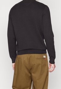 Felpa nera con orlo e polsini a costine, abbinata a pantaloni khaki con tasche posteriori e un'etichetta con il marchio.