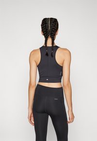 Svart treningscrop-top med racerback-design, med flate sømmer og en tettsittende silhuett, kombinert med svarte høyhalsede leggings.