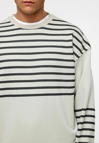 Lichtgrijze sweatshirt met lange mouwen en zwarte horizontale strepen, met een ronde hals en een ontspannen pasvorm, gemaakt van zacht katoen.