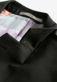 Col de veste noire avec une finition satinée. L'intérieur présente un motif géométrique multicolore dans des teintes pastel. Texture lisse, design ajusté.