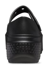 Schwarze Clogs mit einem erhöhten Rücken, aus glattem Material. Sie verfügen über eine strukturierte, gepunktete Sohle und einen markierten Absatz für zusätzlichen Halt.