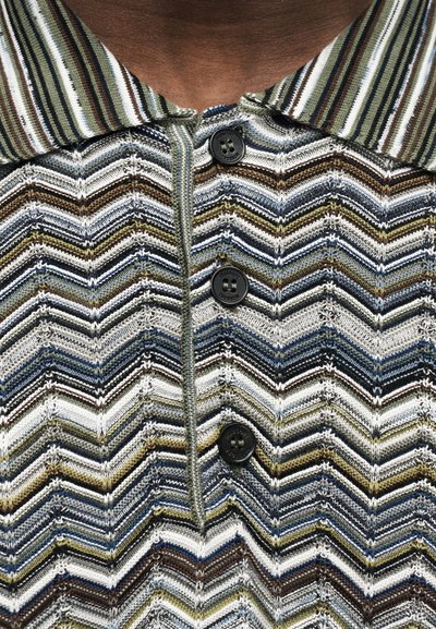 Κοντινό πλάνο πολύχρωμης πλεκτής μπλούζας με σχέδιο σχήματος V, με ριγέ γιακά και τέσσερα μαύρα κουμπιά στο μπροστινό μέρος.