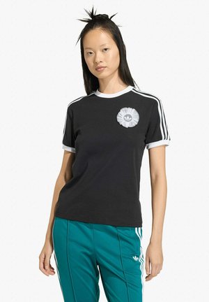 Camiseta negra de manga corta con cuello blanco y tres rayas blancas en cada hombro, con un logo de flor blanca texturizada en el pecho.