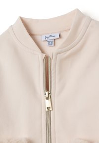 Chaqueta de tela suave en rosa bebé con cremallera plateada y cuello redondeado, tamaño 12-18 meses.
