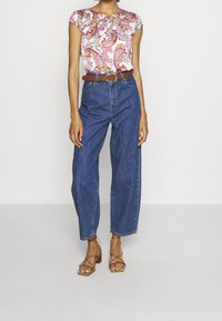 Blomsterkortærmet top i hvid, pink og lilla med rund halsudskæring, parret med højtaljede blå denimjeans og lysebrune strop sandaler.