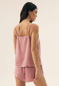 Light pink satin camisole with adjustable straps, paired with matching satin shorts. Smooth texture and loose fit. Minimalist design.