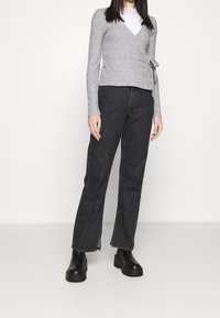 Grå inslagströja med långa ärmar, med ett knyt i midjan, kombinerad med högmidjade svarta jeans och kraftiga svarta stövlar.