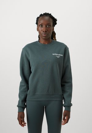 Sweatshirt vert foncé à manches longues, col rond, poignets côtelés et un petit logo blanc sur la poitrine. Texture de tissu lisse.