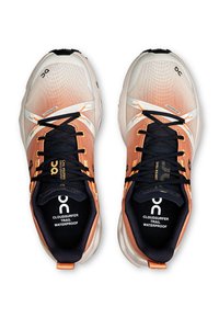 Scarpe da trail running impermeabili con tomaia in rete arancione e crema a gradiente, lacci neri e suole in gomma, con dettagli di logo e branding.