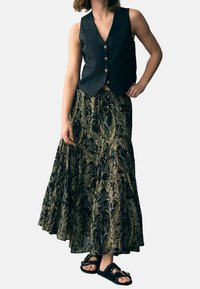 Dunkelblaue ärmellose Weste mit goldenen Knöpfen, kombiniert mit einem langen schwarzen Rock mit Goldmuster und schwarzen Sandalen mit dekorativer Verzierung.