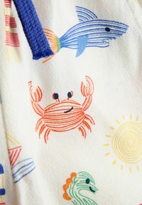 Tessuto bianco con illustrazioni colorate di granchio a strisce, squalo, pesce verde e sole giallo, più una striscia di tessuto blu testurizzato sul lato.