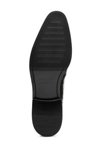 Schwarze Gummisohle mit strukturierter Oberfläche, versehen mit horizontalen Rillen und einem erhabenen Logo "WITTCHEN handmade" an der Ferse.