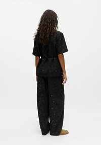 Zwarte outfit met een losse top en brede broek met ingewikkelde bloem- en loofpatronen in donkere tinten. Zachte textuur en ontspannen ontwerp.