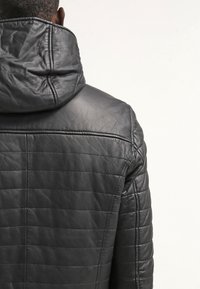 Giacca di pelle nera con design trapuntato, dotata di un colletto alto e una texture liscia, vista dal retro.