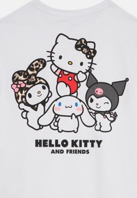 T-shirt en coton blanc avec des personnages de dessin animé de Hello Kitty et ses amis, avec un texte noir en gras disant "HELLO KITTY ET SES AMIS" en dessous.
