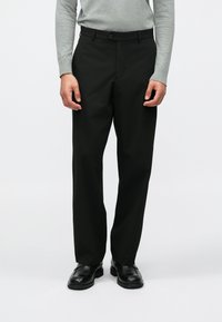 Melni bikses ar pielāgotu piegriezumu, gludu audumu, plakanu priekšpusi, pogu aizdari un sānu kabatām, apvienotas ar pelēku garām piedurknēm.