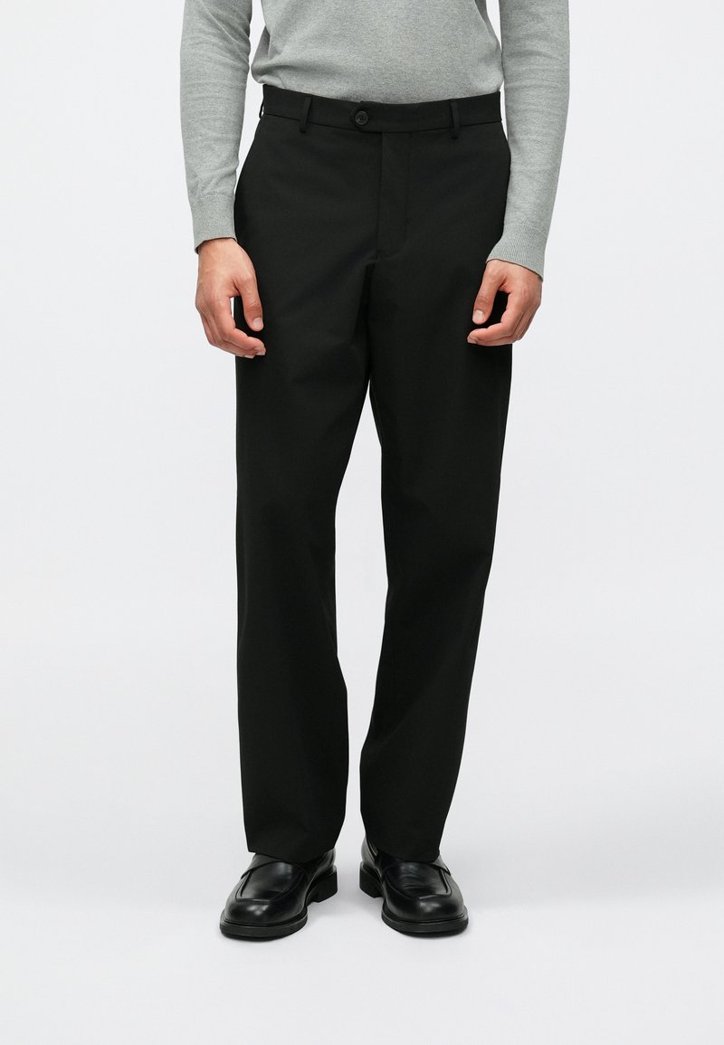 Melni bikses ar pielāgotu piegriezumu, gludu audumu, plakanu priekšpusi, pogu aizdari un sānu kabatām, apvienotas ar pelēku garām piedurknēm.