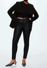 Zwarte stretchjeans met een slim fit, gedragen met een zwart crop-top en een oversized blazer, aangevuld met puntige zwarte slingback hakken met studs.