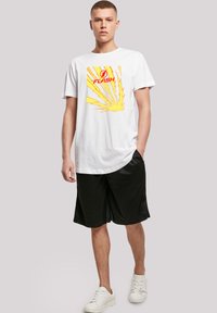 Hvid bomuldst-shirt med et rødt "FLASH" logo og et gult lyn-design, parret med sorte shorts og hvide sneakers.