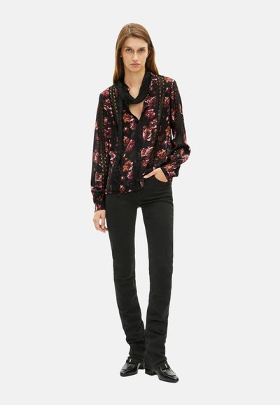 Blusa nera a fiori con maniche lunghe, caratterizzata da dettagli in pizzo, abbinata a pantaloni neri aderenti e scarpe a punta quadrata.