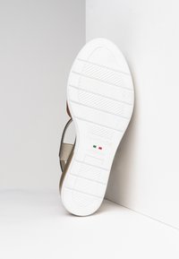 Suela de goma blanca con patrón texturizado, con un diseño de correas en gris y dorado. Nombre de la marca "NeroGiardini" estampado cerca del talón.