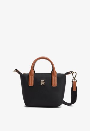 Zwarte stoffen draagtas met handgrepen en riem van lichtbruin leer, gouden logodetail aan de voorkant, compacte vorm en gladde textuur.