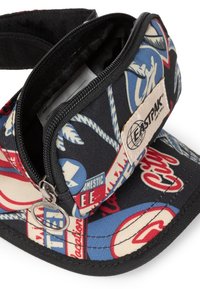 Black cap with zippered pocket, featuring a multicolored graphic pattern of logos and text. Material is durable fabric with contrasting stitching.