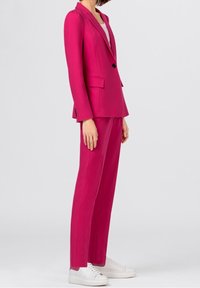 Fuchsiový oblek se sestává z upravené blazer a kalhot rovného střihu, vyrobený z hladké tkaniny, s jedním knoflíkem a předními kapsami. Bílé tenisky.
