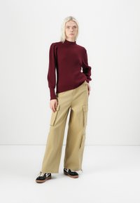 Burgundy ribbed knit sweater with a high neckline, paired with beige wide-leg cargo pants featuring multiple pockets. Black sneakers with white accents.