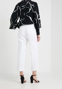 Svart blus med vitt abstrakt mönster, kombinerad med vita raka byxor. Svarta klacksandaler fulländar outfiten.