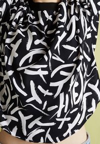 Haut en tissu noir présentant un motif audacieux de coups de pinceau blancs abstraits. Design froncé avec un col élastique pour un ajustement décontracté.