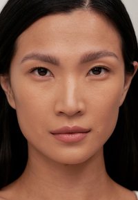 Primer plano de un rostro con piel suave, cabello oscuro y maquillaje natural. Las características incluyen ojos oscuros y cejas suavemente definidas, con un color de labios neutro.