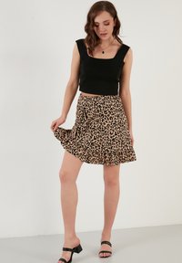 Zwart cropped top met brede bandjes, gecombineerd met een flared beige rok met een zwart luipaardprint en gelaagde ruches. Zwarte haksandalen.
