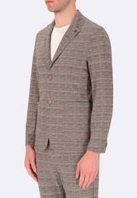 Blazer marrone con texture e un leggero motivo a quadri, due bottoni e revers a notched, abbinato a una camicia di colore chiaro sotto.