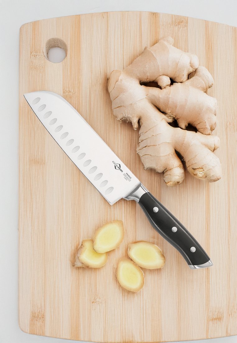 Coltello da chef in acciaio inossidabile con manico nero, dotato di tre rivetti e una lama a regolazione cava, posizionato su un tagliere di legno con fette di zenzero.