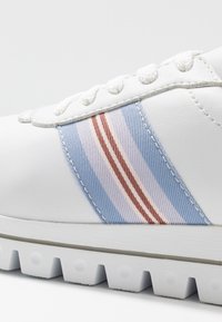 Sneaker bianco con una superficie in pelle liscia, dettagli a strisce blu chiaro e rosa, e una suola in gomma testurizzata con scanalature.