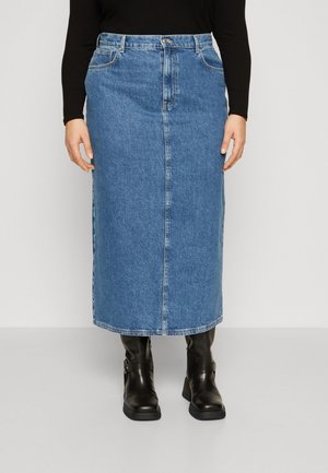 Kvinde iført en blå denim midi nederdel med frontsøm, en sort langærmet top og sorte ankelstøvler med spænder.