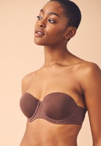 Soutien-gorge marron sans bretelles avec une texture lisse, des coques moulées, des baleines pour le soutien et des détails de couture subtils. Convient à des tenues diverses.